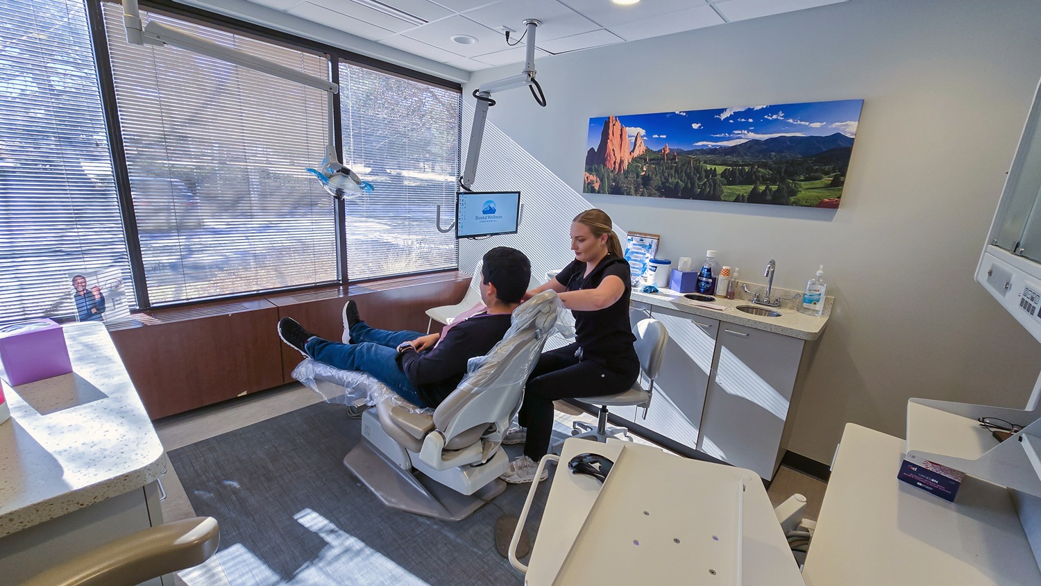 Treatment room at Dental Wellness Centennial with a patient settling in beside a team member